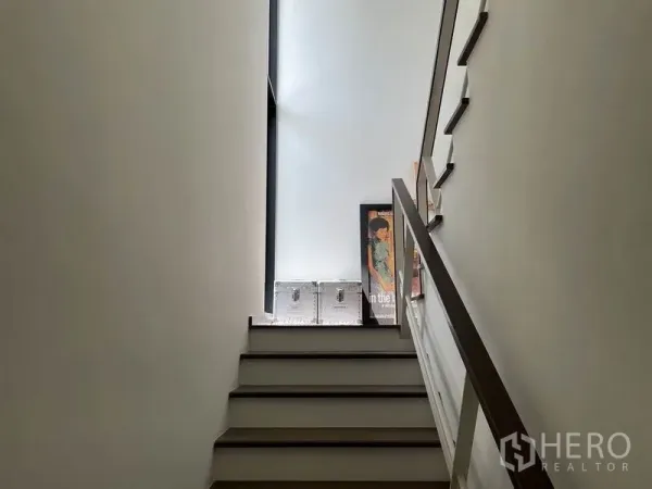 Detached House for sale in Sai Mai, Bangkok - Bright stairwell with a high window, white walls and a wooden handrail.