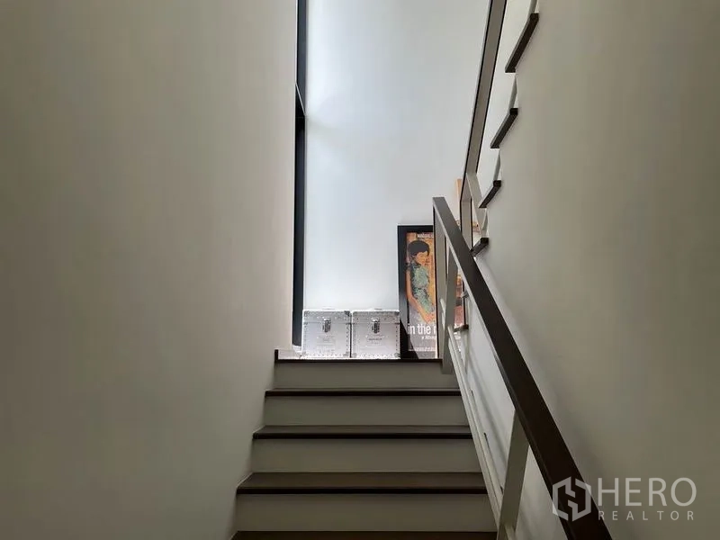 Detached House for sale in Sai Mai, Bangkok - Bright stairwell with a high window, white walls and a wooden handrail.