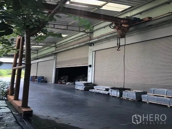 Factory for sale in Khlong Luang, Pathum Thani - Row of roller‑shutter doors beside a sheltered loading zone equipped with a hoist.