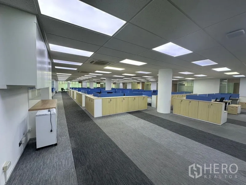 Office Space for rent - Wide workspace with columns, blue-divider desks and natural light from large windows.