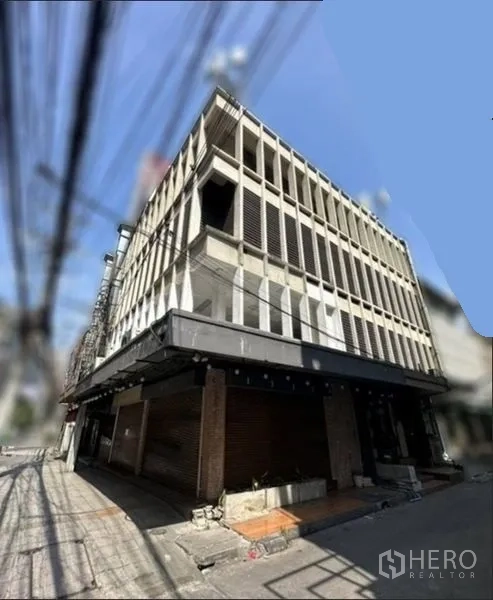 Shophouse for rent in Khlong Toei, Bangkok - Corner perspective of a multi-storey shophouse building with a grid-pattern concrete exterior and wide awning.
