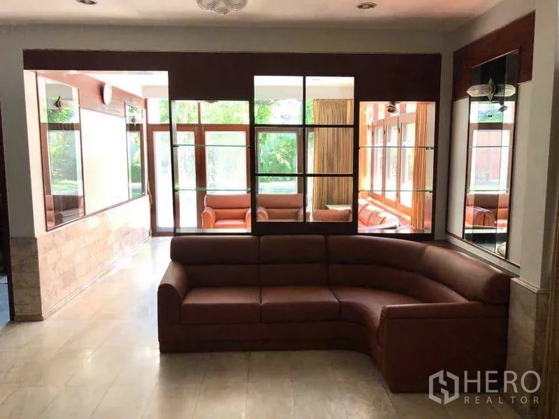 Detached House for rent in Phra Khanong, Bangkok - Bright living area with curved leather sectional, large windows and tiled floors.