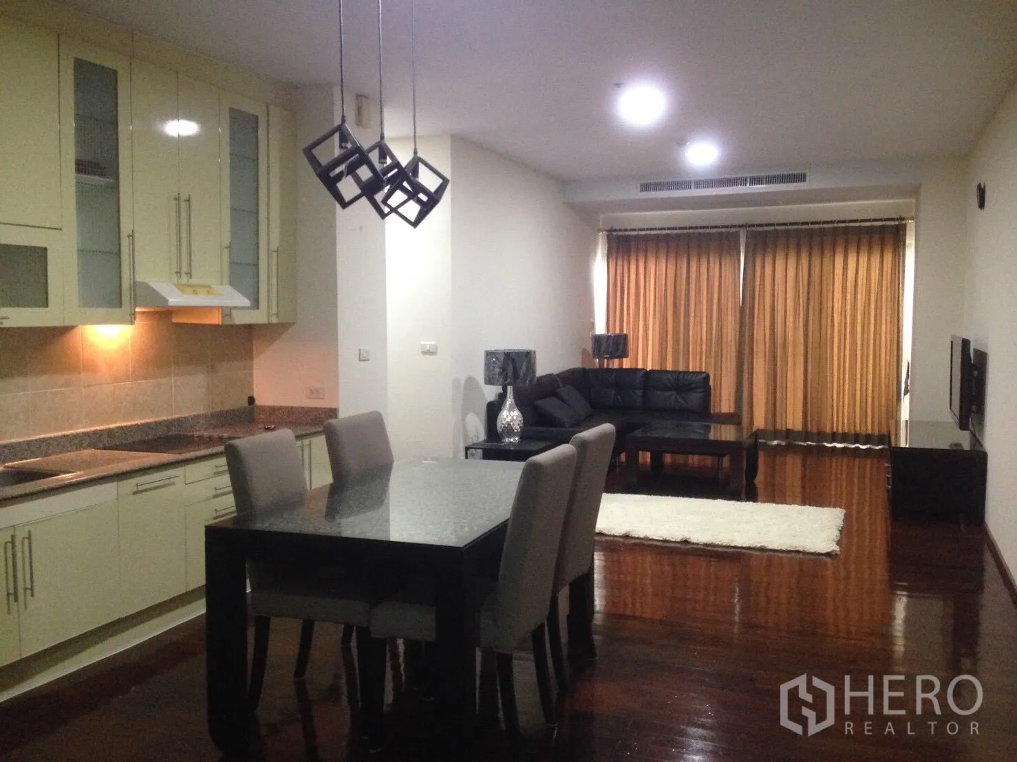 公寓 出租在Watthana, Bangkok - 开放式客餐厅，带整体厨房、几何吊灯和黑色皮沙发。