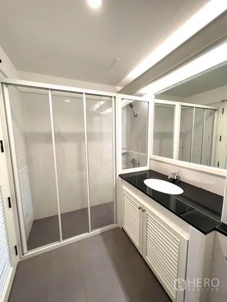 公寓 出租在Watthana, Bangkok - 第二浴室配玻璃干湿分离淋浴区、宽镜面与白色洗手台黑色台面。