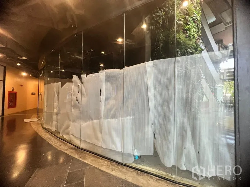 Retail Space for rent - Curved full-height glass storefront along an indoor mall corridor with temporary coverings and warm ceiling lights.