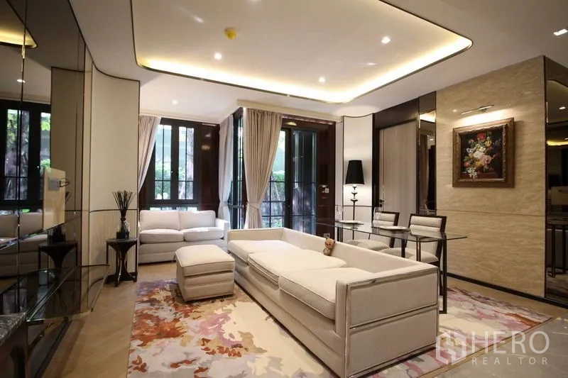 公寓 出租在Watthana, Bangkok - 雅致客厅，白色沙发、嵌灯吊顶、落地窗与玻璃餐桌，望向绿景。