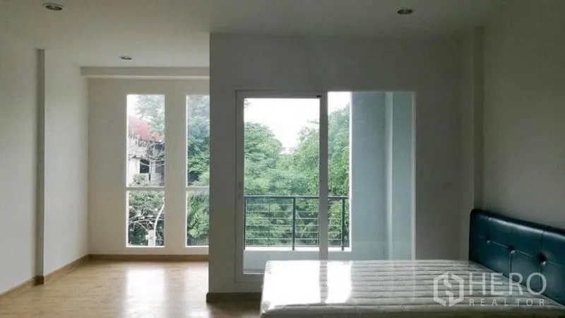 联排别墅 出租在Wang Thonglang, Bangkok - 宽敞卧室，大窗与阳台门，可见绿树景观