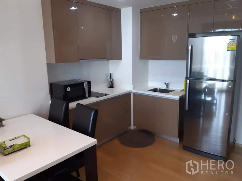 Condominium for rent in Khlong Toei, Bangkok - Modern kitchenette with glossy cabinets, cooktop, and stainless fridge in a Sukhumvit condo.