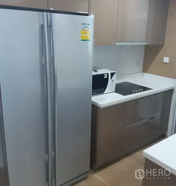 Condominium for rent in Khlong Toei, Bangkok - Modern condo kitchen with side-by-side fridge, microwave and built-in electric cooktop.