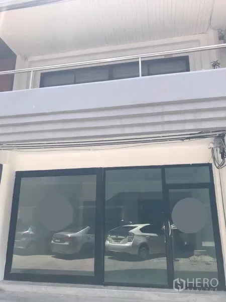 Retail Space for rent in Watthana, Bangkok - Street-level retail facade with full-width black-framed glass sliding doors and balcony above, cars reflected in the glass.