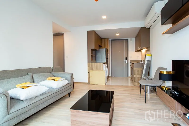 公寓 出租在Watthana, Bangkok - 开放式起居区，灰色沙发、木地板，配备小厨房、冰箱与洗衣机