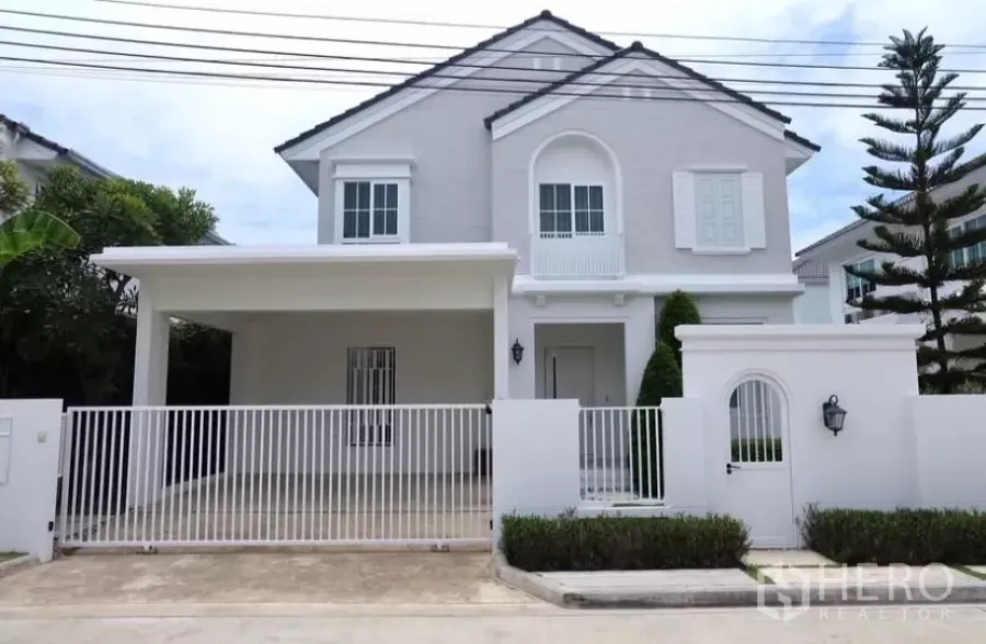 独立式住宅 出租在Bang Phli, Samut Prakan - 白色两层独栋别墅，带前院铁门与有顶车位，社区宁静。