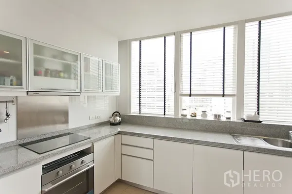 Condominium for rent in Khlong Toei, Bangkok - Modern U-shaped kitchen with white cabinets, granite countertops, and large windows.
