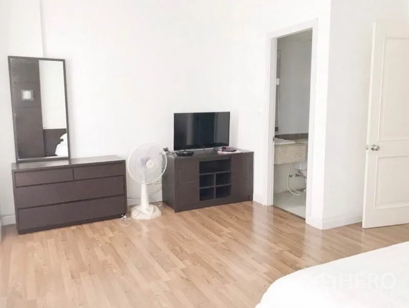 联排别墅 出租在Prawet, Bangkok - 卧室一角，五斗柜、电视柜、落地扇，并有套内卫浴的门。