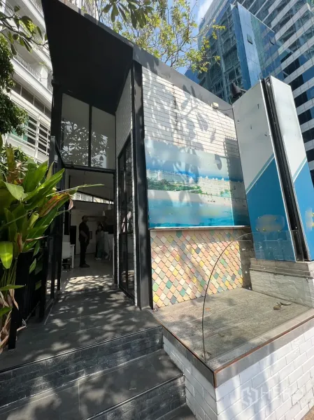 Retail Space for rent in Pathum Wan, Bangkok - Modern retail kiosk-style entrance with white brick walls, glass façade and city tower backdrop under shade trees.