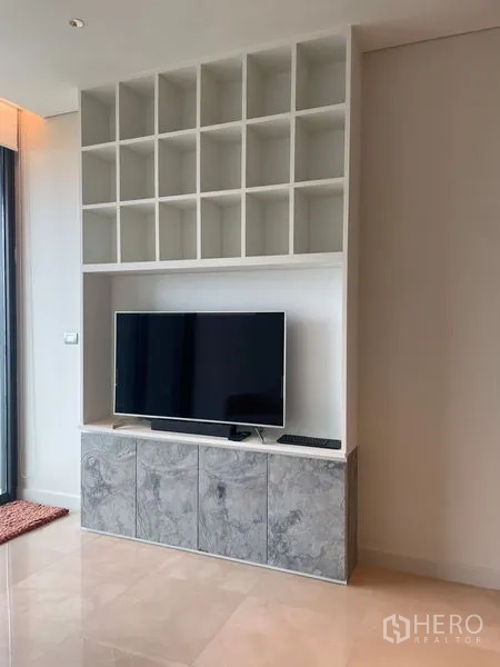 Condominium for rent in Pathum Wan, Bangkok - Custom TV wall with open display cubbies and marble-finish base cabinets.