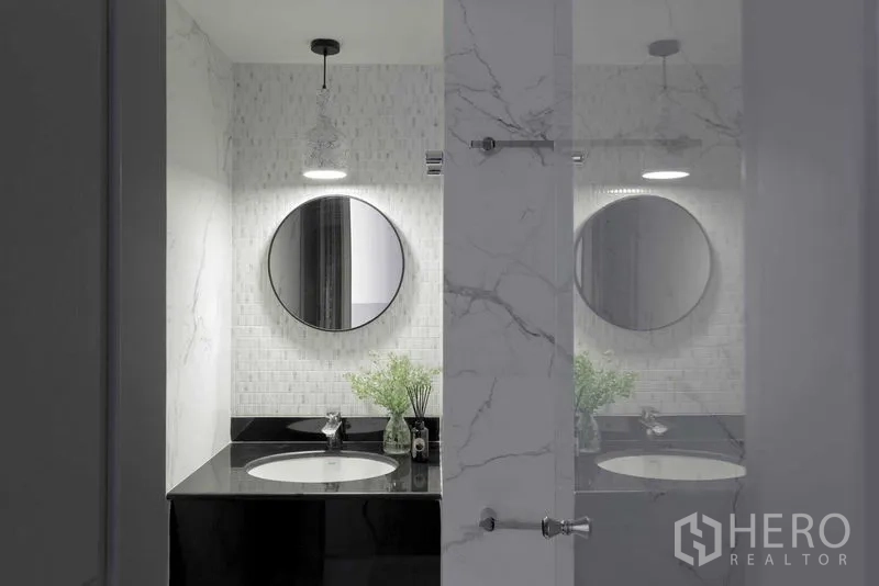 Condominium for sale in Watthana, Bangkok - Modern bathroom with round mirror, black countertop and marble-look walls.