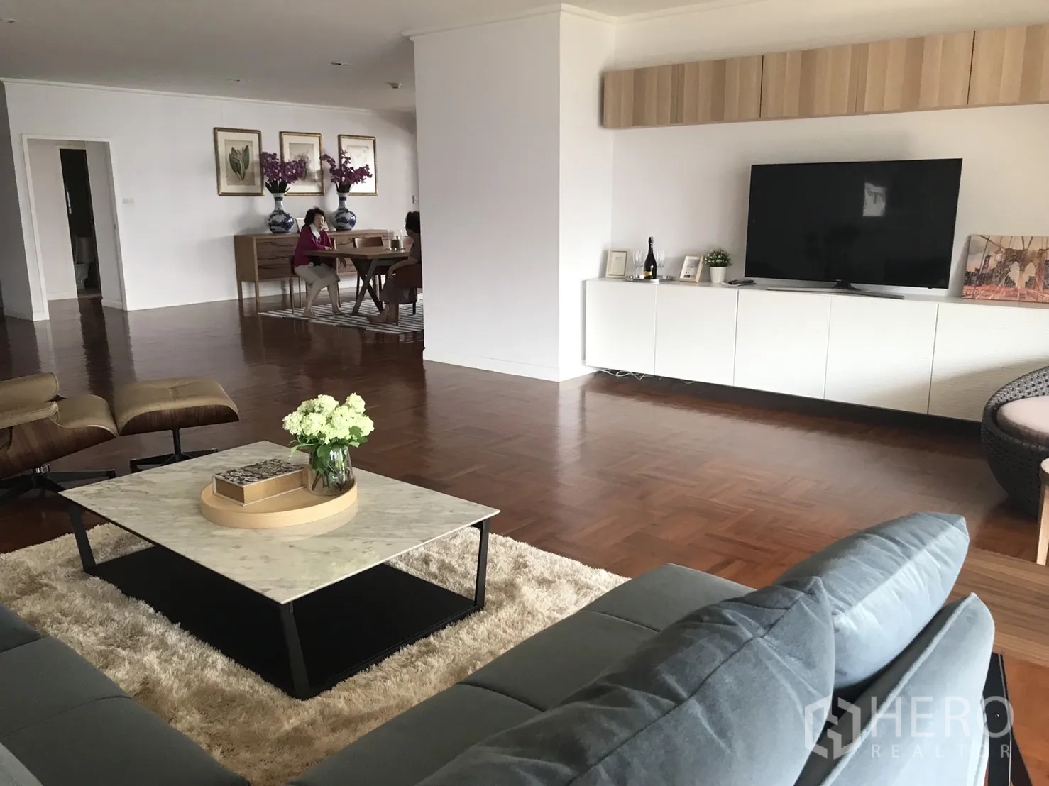 Condominium for rent in Bangkok - Open-plan lounge with wall-mounted TV console, marble coffee table, and view into the dining area.