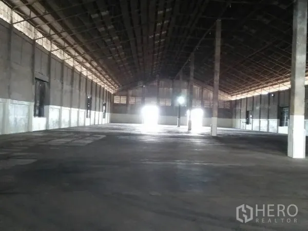 货栈 出租在Pathum Thani - 宽敞仓库内部，高钢结构屋顶、混凝土地面与中心立柱，装卸门采光明亮。