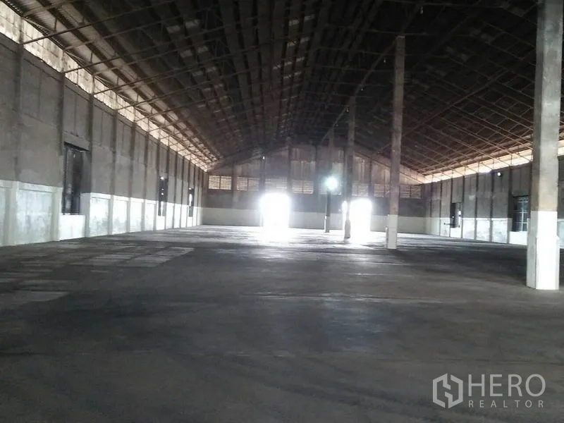 货栈 出租在Pathum Thani - 宽敞仓库内部，高钢结构屋顶、混凝土地面与中心立柱，装卸门采光明亮。