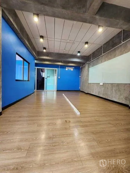 办公空间 出租或出售在Bueng Kum, Bangkok - 明亮工作间，木地板、蓝色强调墙、顶灯，并配玻璃门通往会议室。