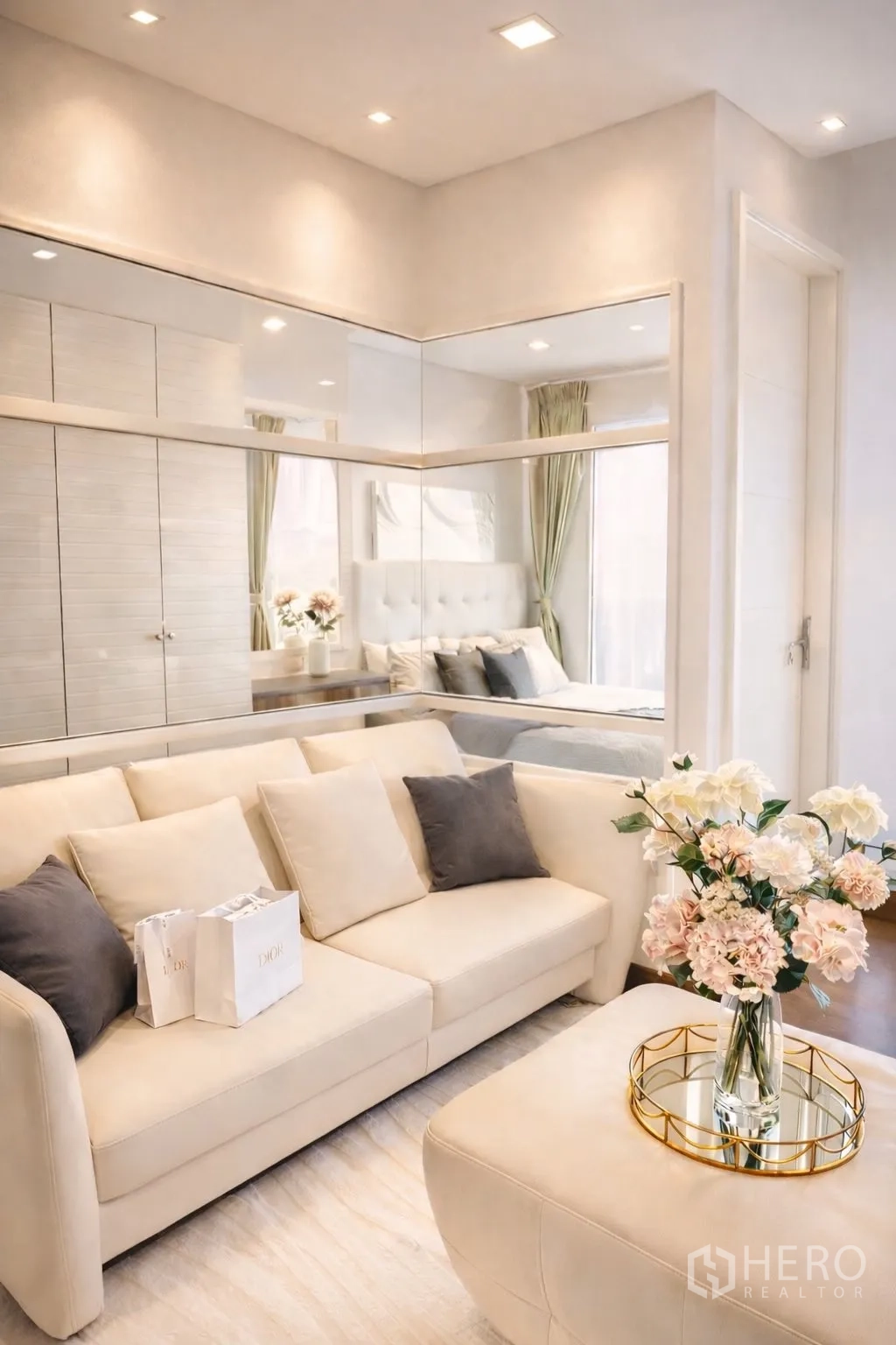 คอนโด for rent or sale in Watthana, Bangkok - ห้องนั่งเล่นสว่างด้วยโซฟาสีครีม ผนังกระจกเงา และแจกันดอกไม้ ข้างฉากกั้นกระจกห้องนอน