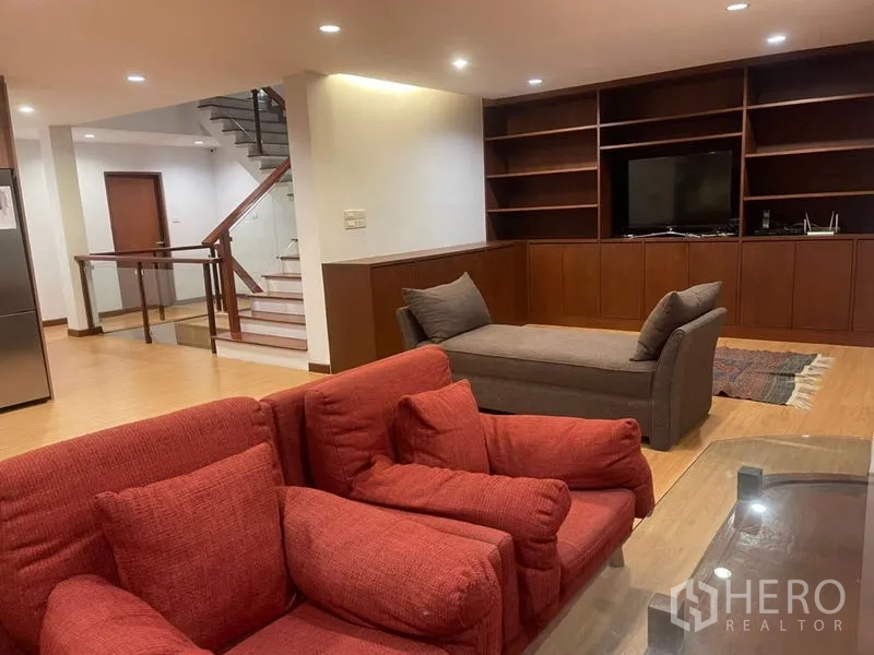 Townhouse for rent in Suan Luang, Bangkok - Spacious family room with built-in media wall, shelving, wood floors and staircase.