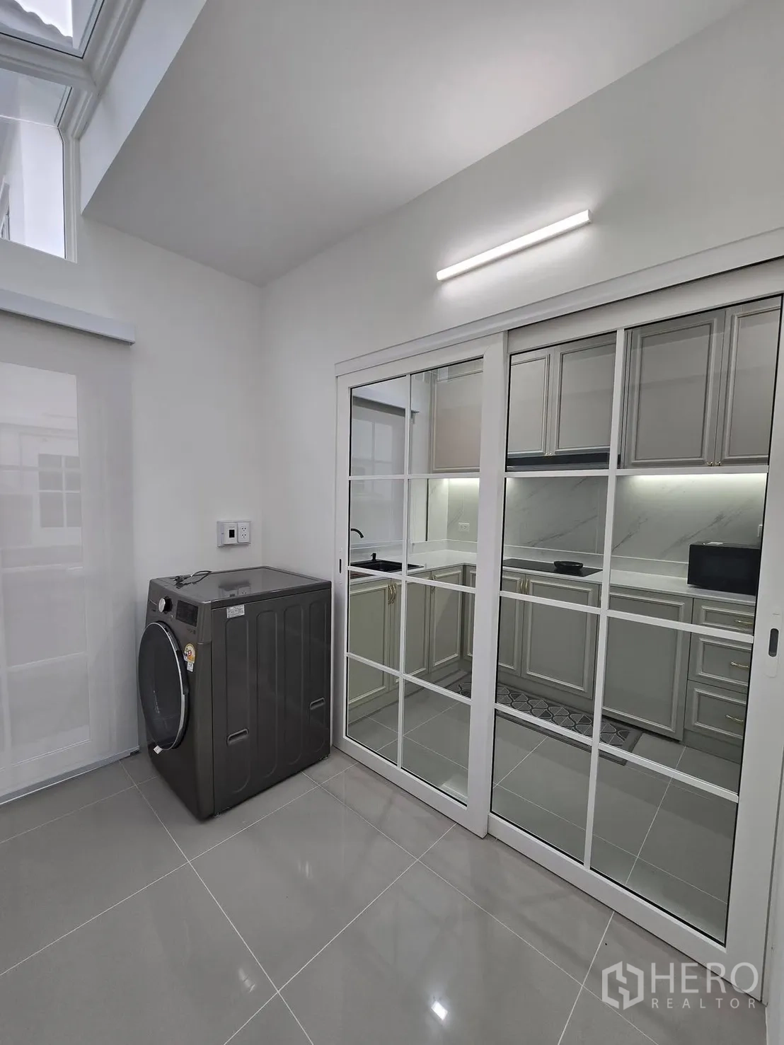 Semi-detached House for rent in Mueang Samut Prakan, Samut Prakan - Laundry area with front-load washer, skylight roof and glass sliding doors to the kitchen.
