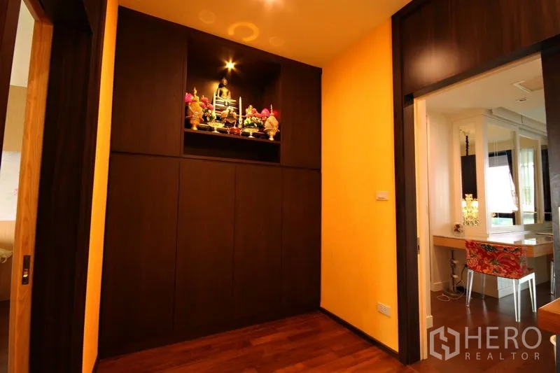 Condominium for rent or sale in Khlong Toei, Bangkok - Hallway with an illuminated built-in shrine cabinet and warm accent wall.
