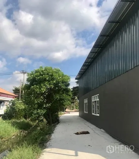 货栈 出租在Lam Luk Ka, Pathum Thani - 仓库侧边人行道，外墙有窗，旁有小渠与绿化。