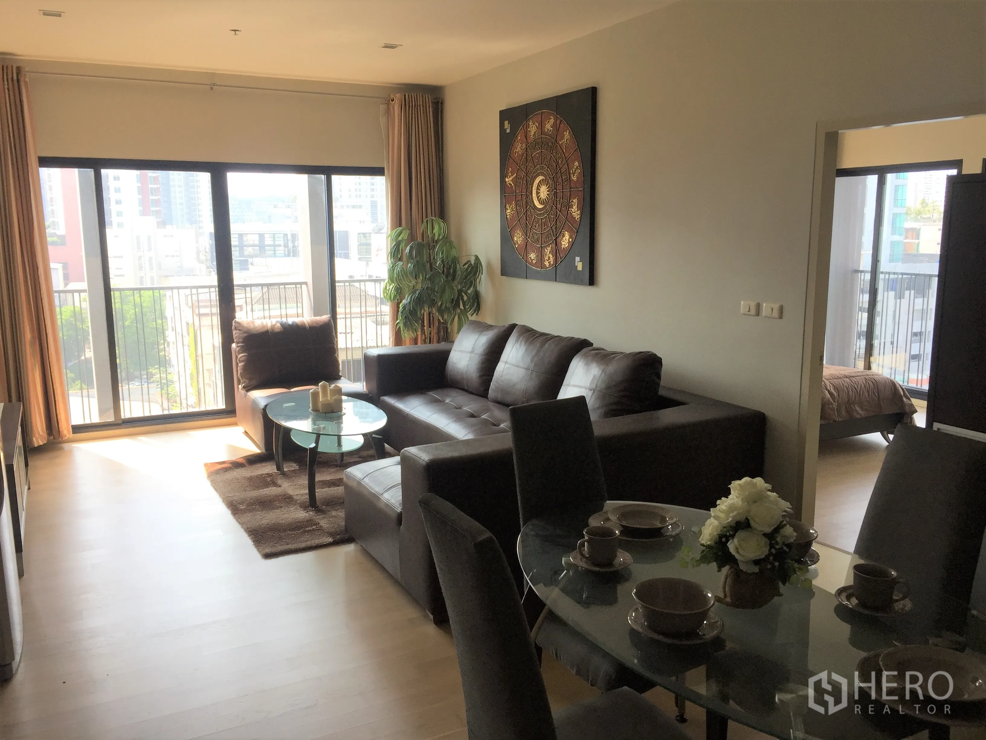 Condominium for rent in Watthana, Bangkok - Open‑plan living and dining area with dark leather sofa, glass coffee table and wide sliding windows to the city.
