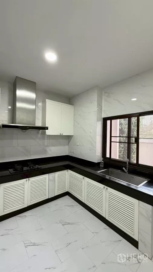 独立式住宅 出售在Saphan Sung, Bangkok - 明亮L型厨房，白色橱柜、黑色台面、燃气灶与不锈钢烟机