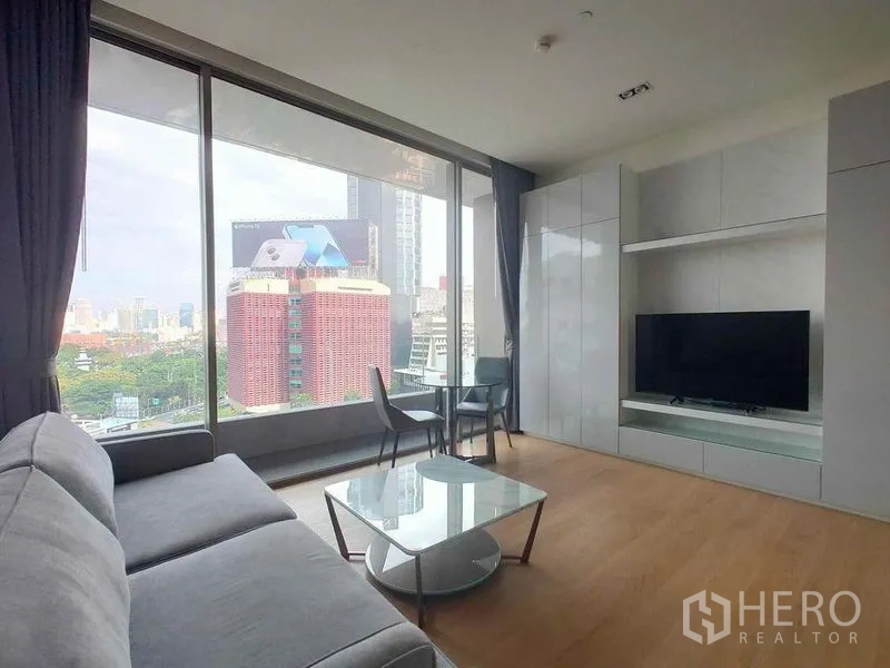 公寓 出租在Bang Rak, Bangkok - 客厅设电视墙、沙发与茶几，落地窗外是城市建筑景观。