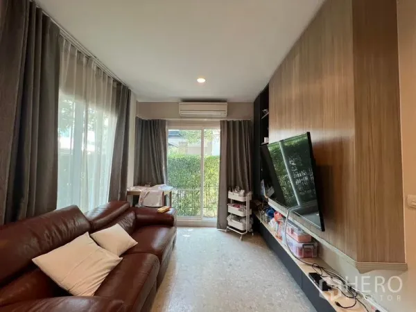 Detached House for rent or sale in Saphan Sung, Bangkok - Cozy living room with brown leather sofa, TV wall and sliding glass doors.