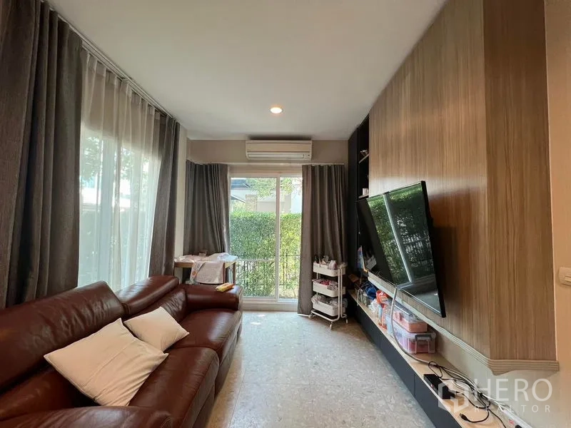 Detached House for rent or sale in Saphan Sung, Bangkok - Cozy living room with brown leather sofa, TV wall and sliding glass doors.