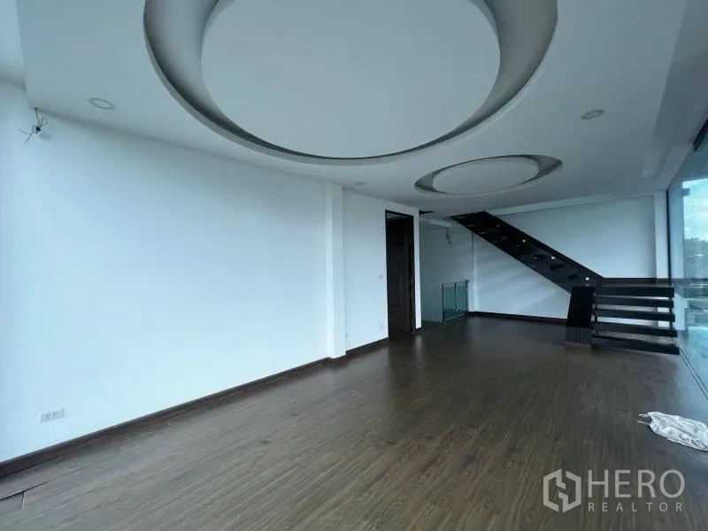 独立式住宅 出售在Lat Phrao, Bangkok - 二层宽敞起居室，木地板、圆形吊顶与玻璃墙旁楼梯。