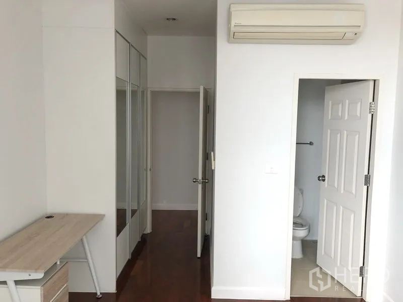 Condominium for rent in Khlong Toei, Bangkok - Bedroom featuring a study desk, mirrored wardrobes, and an entrance to an ensuite bathroom.