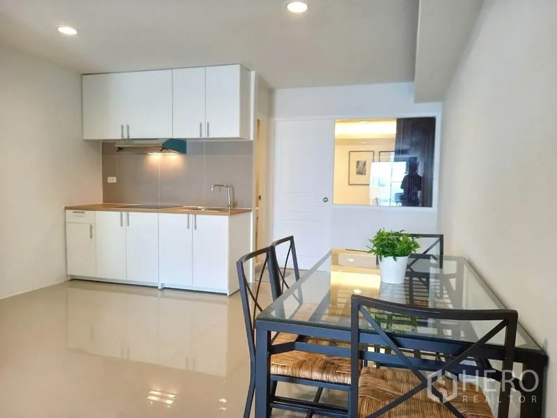 Condominium for rent in Khlong Toei, Bangkok - Glass-top dining set beside a compact white kitchenette with overhead cabinets.