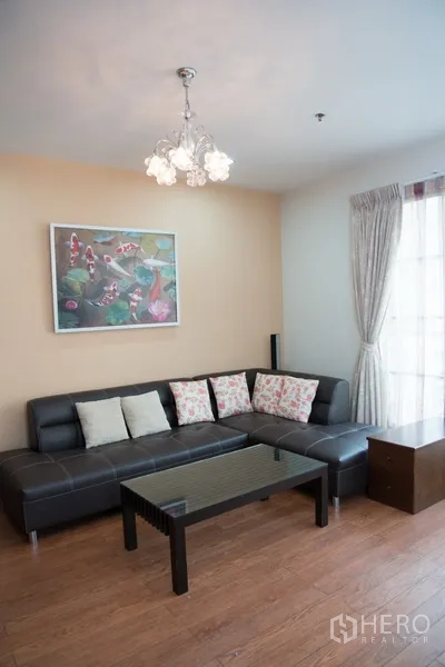 Condominium for rent in Khlong Toei, Bangkok - Cozy lounge corner with black sectional sofa, glass coffee table and chandelier against wood flooring.