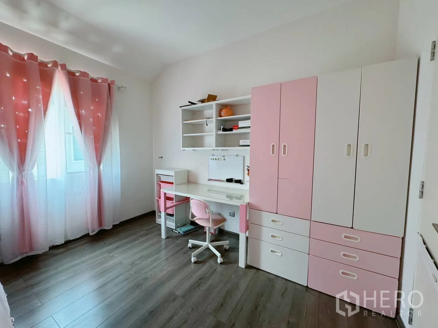 บ้านเดี่ยว for rent or sale in Bang Phli, Samut Prakan - ห้องเด็กหรือห้องทำงานสว่างด้วยผ้าม่านสีชมพู ตู้เสื้อผ้าขาวชมพู และโต๊ะทำงาน พื้นไม้