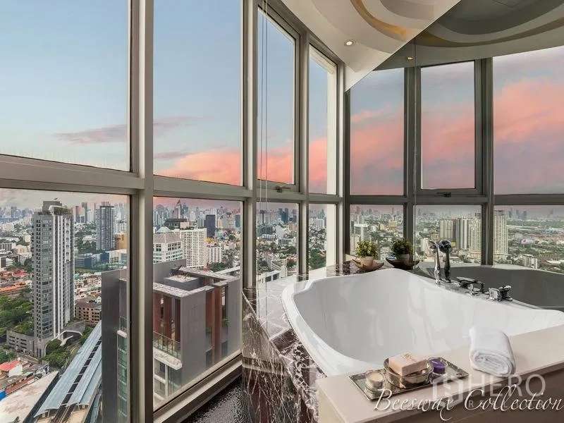 Condominium for rent in Watthana, Bangkok - Corner bathtub beside wraparound floor‑to‑ceiling windows offering sunset skyline views over Bangkok.