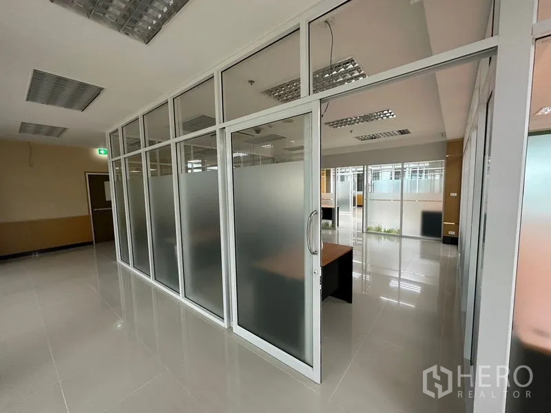 Office Space for rent in Suan Luang, Bangkok - Hallway with glass-partitioned offices and sliding doors leading to bright, modern work areas.
