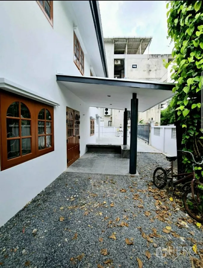 带办公室的家 出租在Lat Phrao, Bangkok - 门廊设有雨棚，碎石庭院与木质双开大门旁的长凳。