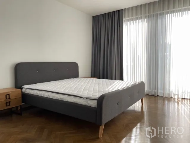 独栋房屋 for rent in Watthana, Bangkok - 宽敞卧室，灰色床、人字拼地板与落地窗。