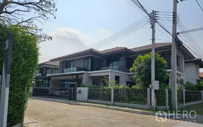 Detached House for sale in Lam Luk Ka, Pathum Thani - Wide street view of the residence with balconies, greenery and tiled roof.