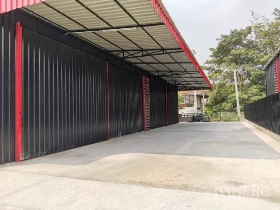 Warehouse for rent in Wang Thonglang, Bangkok - Black and red steel warehouse exterior with a wide concrete driveway and deep covered loading bay in Wang Thonglang, Bangkok.