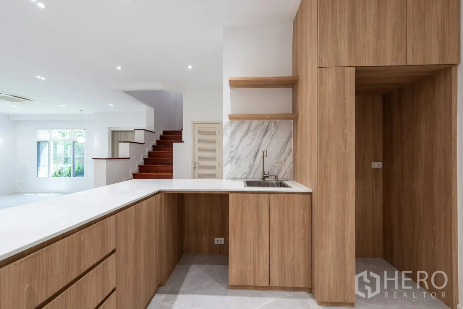 Detached House for sale in Bang Phli, Samut Prakan - Open kitchen with wood cabinetry, white countertops and a nearby staircase.