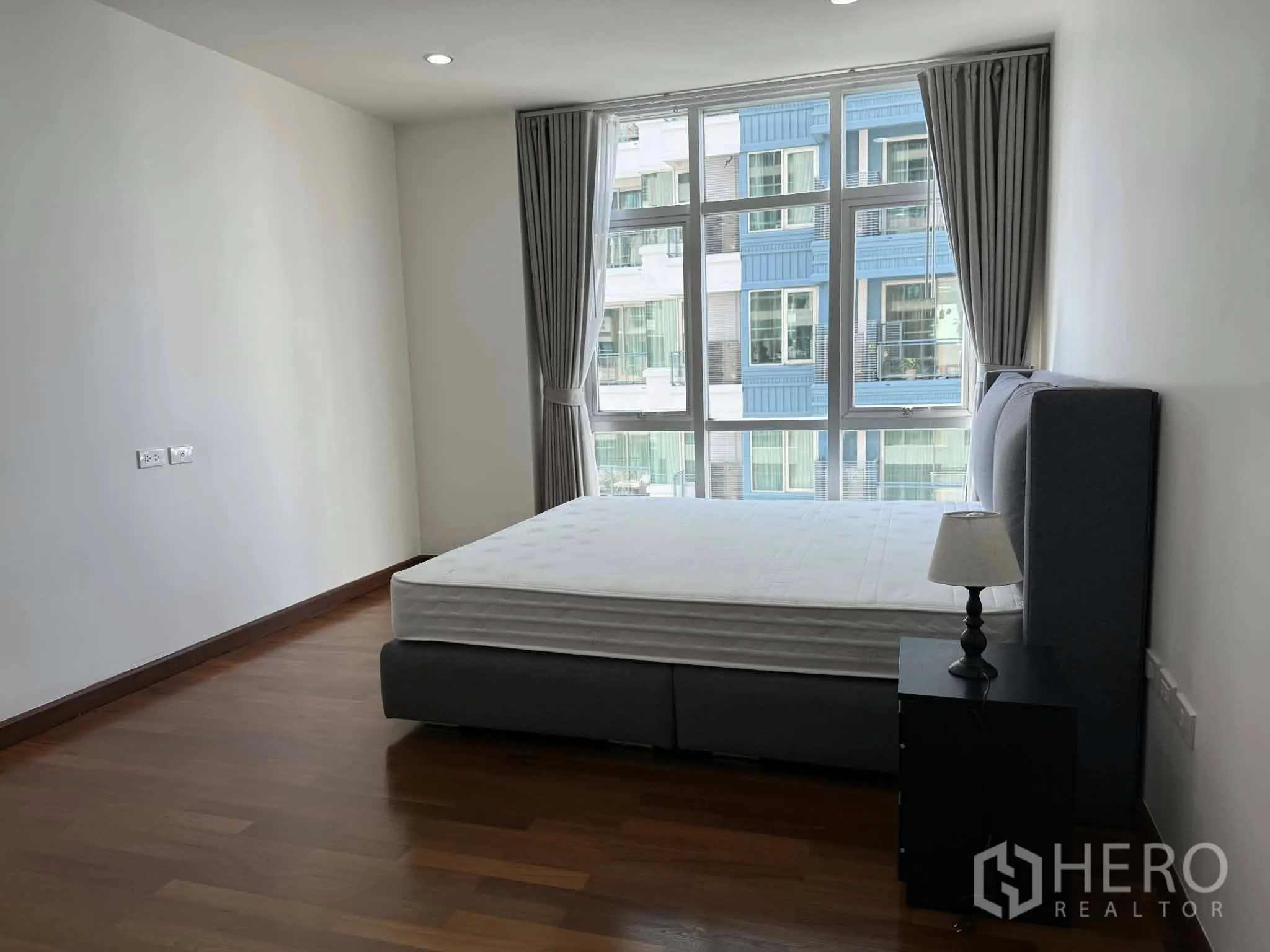 Condominium for rent in Pathum Wan, Bangkok - Bedroom with upholstered bed, bedside table, and large windows.
