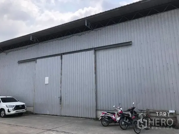 Warehouse for rent in Pak Kret, Nonthaburi - Corrugated metal warehouse exterior with large sliding doors and onsite parking in Pak Kret.