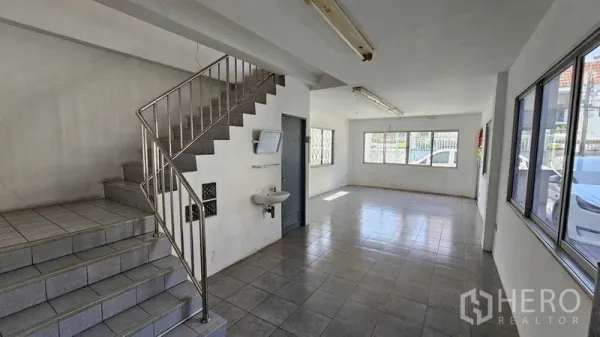 Warehouse for rent in Lak Si, Bangkok - Bright ground-floor warehouse office with tiled flooring, staircase, and large windows.
